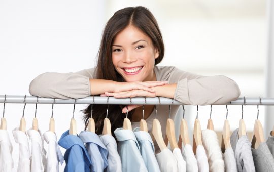 Business owner - clothes store. Young female business owner in her shop behind clothes rack smiling proud and happy. Multicultural Caucasian / Asian female model.